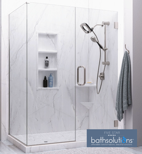 Frameless glass walk-in shower with light gray marble-look wall surrounds, built-in recessed shelf niche holding soap and shampoo bottles, a dual handheld shower head combo on a vertical slide bar, brushed metal handle, and Five Star Bath Solutions logo in the bottom right corner.