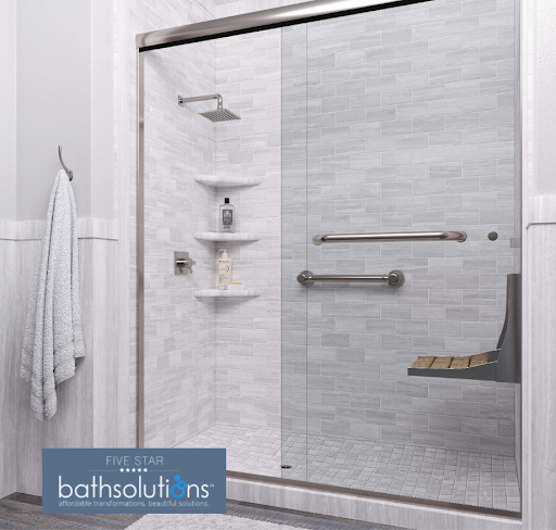Walk-in shower featuring a sliding glass door, light gray subway tile pattern surround, overhead square rain shower head, corner shelves, safety grab bars, fold-down wooden-style bench seat, and Five Star Bath Solutions logo in the bottom left corner.